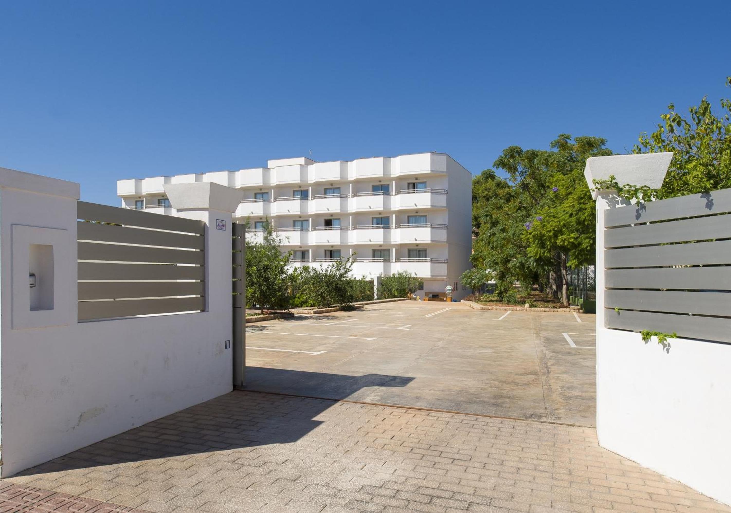 A gated entrance to a multi-story residential building with a paved driveway and greenery.
