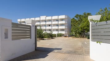 A gated entrance to a multi-story residential building with a paved driveway and greenery.