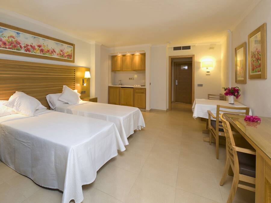Habitación de hotel con dos camas, un escritorio con televisor, una pequeña cocina y una mesa de comedor.