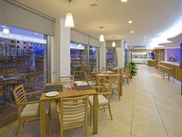 A restaurant with wooden tables and chairs, large windows, and a bar area.
