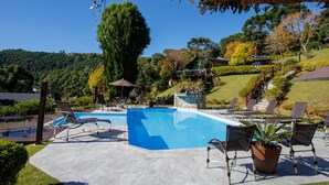 A pool area with lounge chairs, a stone planter, and a thatched roof structure. - Pousada Varanda das Colinas (Monte Verde)
