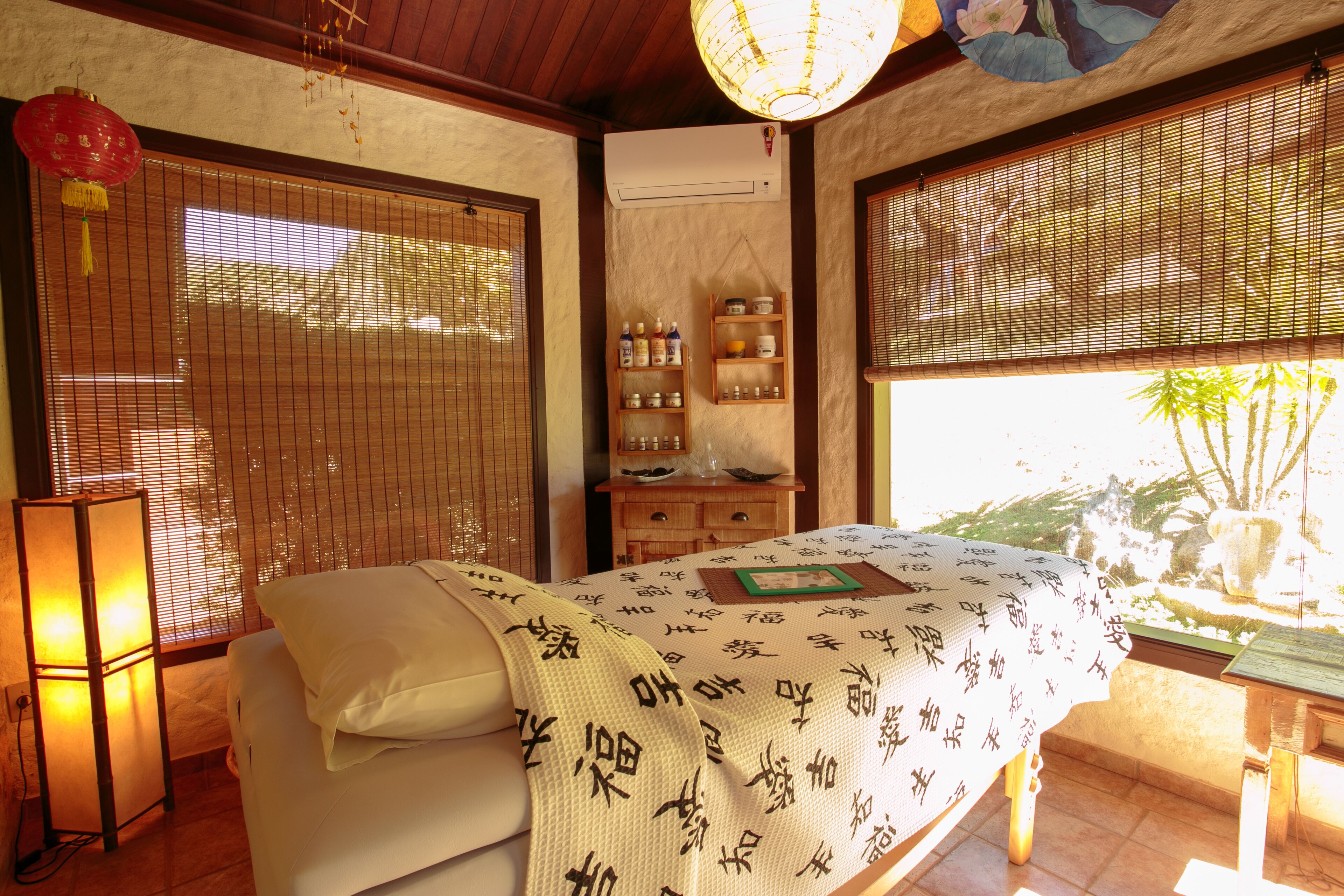 A traditional Japanese-style room with tatami flooring, a bed with a white bedspread featuring calligraphy, a wooden cabinet with bottles, and a sliding door with a view of greenery outside.
