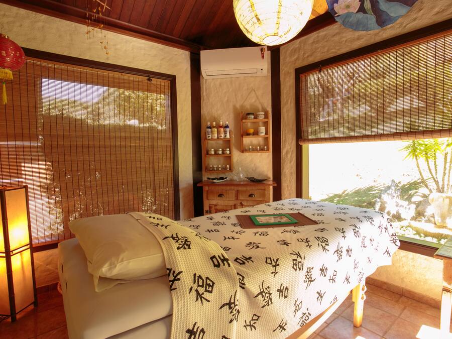 A traditional Japanese-style room with tatami flooring, a bed with a white bedspread featuring calligraphy, a wooden cabinet with bottles, and a sliding door with a view of greenery outside.