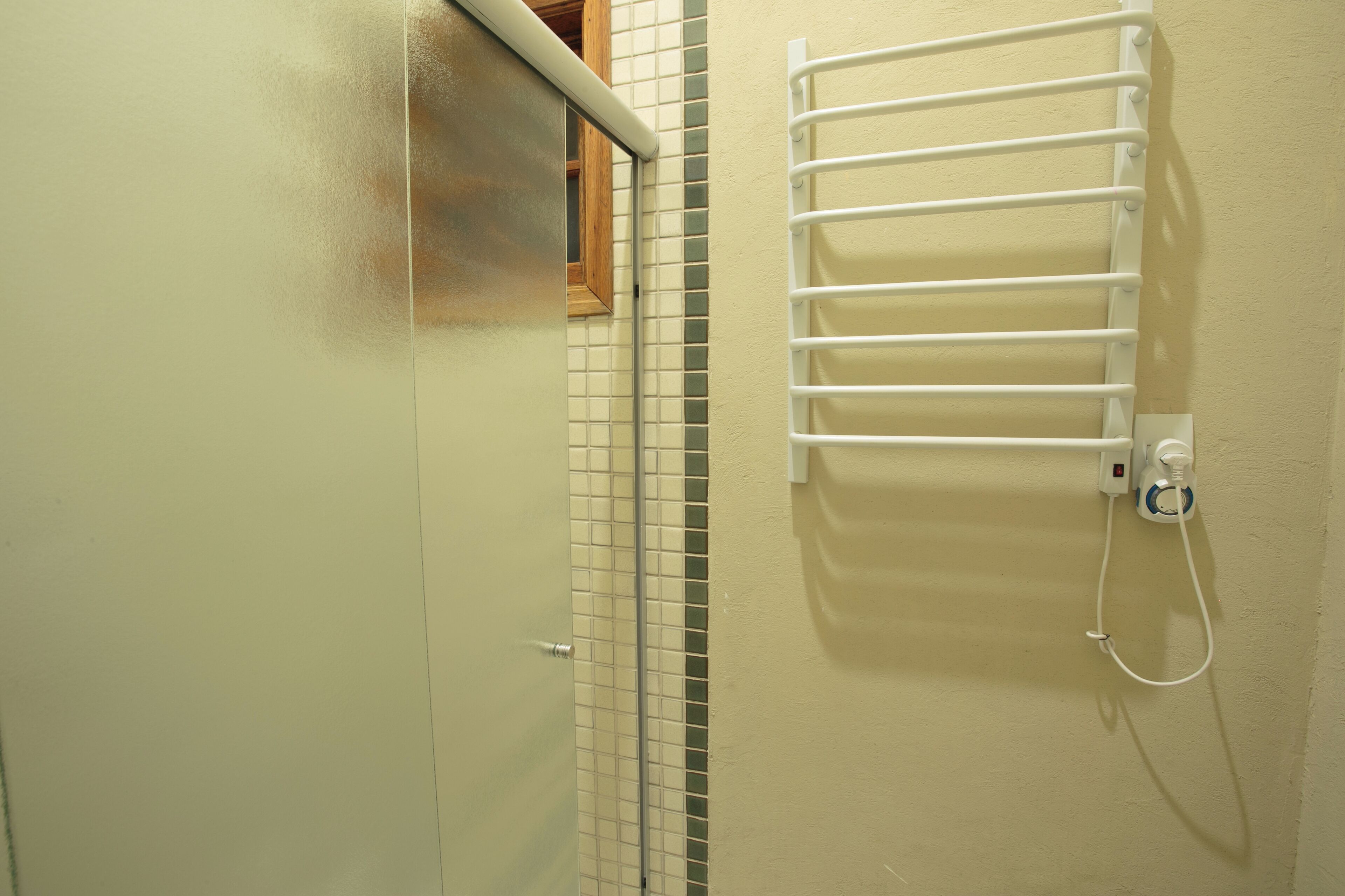 A bathroom with a tiled wall, a white towel rack, and a shower control panel.