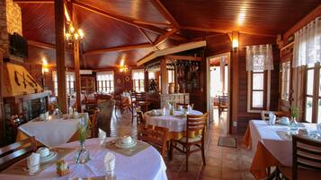 Restaurante com interiores em madeira, várias mesas de jantar com toalhas brancas e uma variedade de cadeiras.