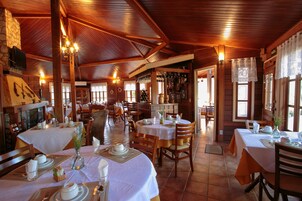 Restaurante com interiores em madeira, várias mesas de jantar com toalhas brancas e uma variedade de cadeiras.