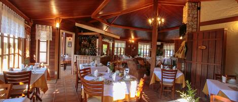 A restaurant with wooden interiors, multiple tables and chairs, and a bar area.