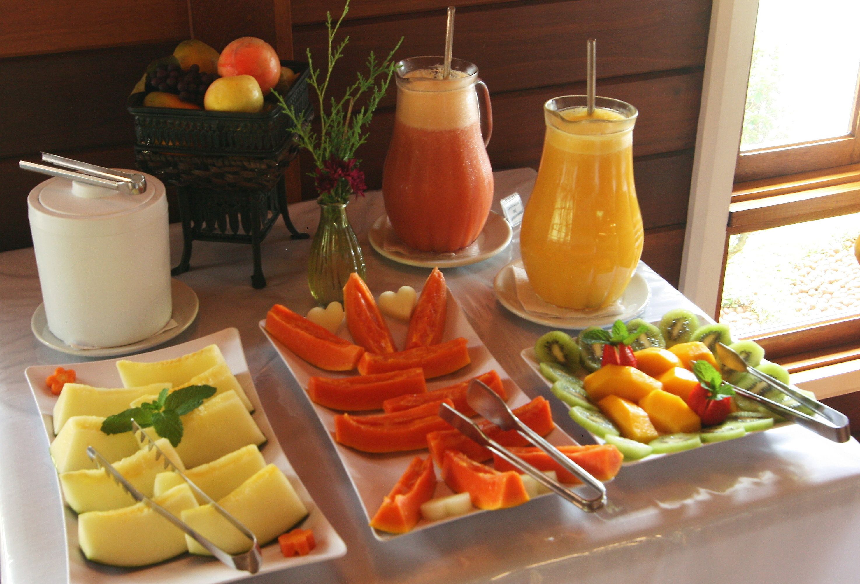 Un buffet de petit-déjeuner avec divers fruits, une carafe de jus d’orange et un verre de smoothie.
