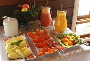 A breakfast buffet with various fruits, a pitcher of orange juice, and a glass of smoothie. - Pousada Varanda das Colinas (Monte Verde)