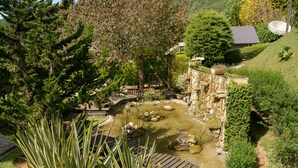 A garden with a pond, stone walls, and a wooden deck. - Pousada Varanda das Colinas (Monte Verde)