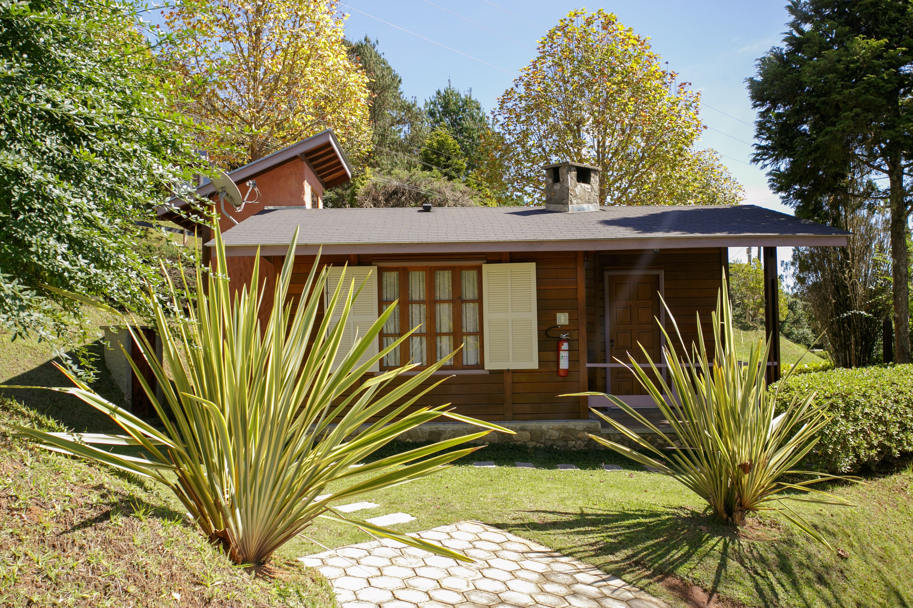 Een houten chalet met een schuin dak, omgeven door een tuin met agaveplanten en een pad van stenen.