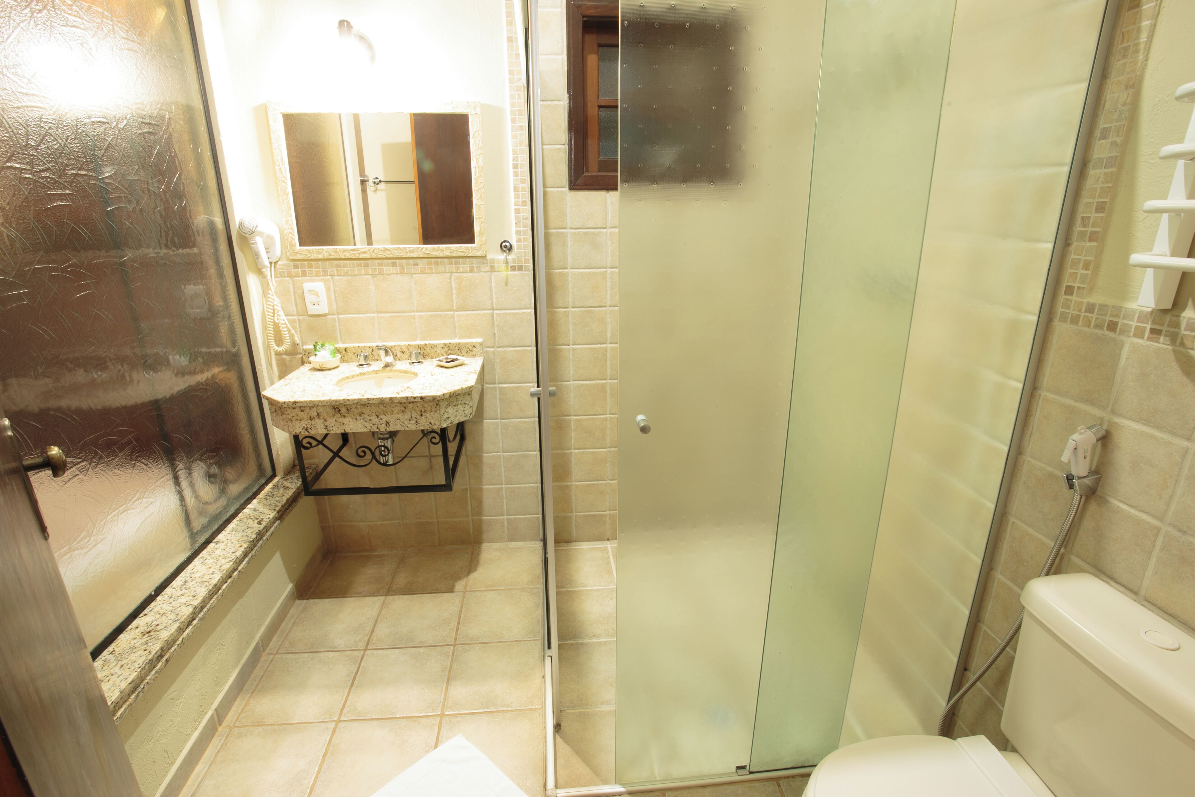 Un baño con ducha envuelta en vidrio, un lavamanos con un revestimiento de azulejos decorativos y un inodoro.