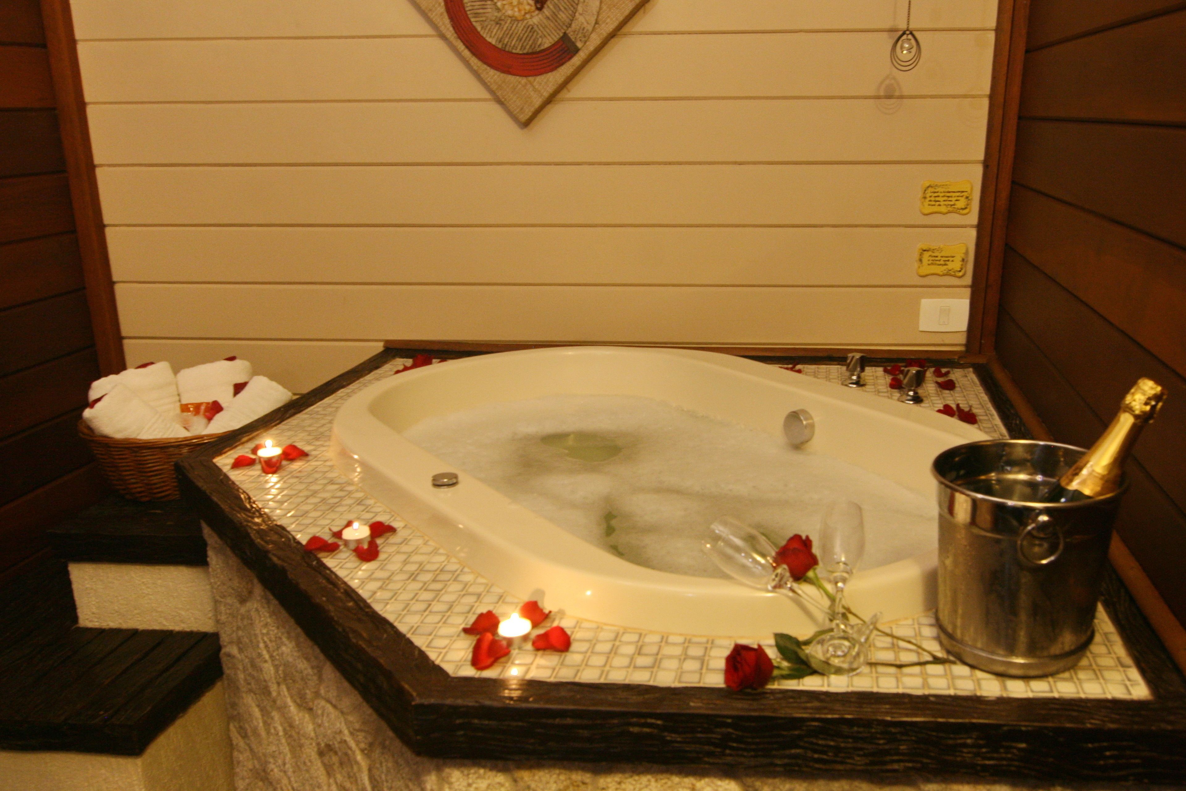 A hot tub with rose petals and candles, a champagne bottle, and a basket of towels.
