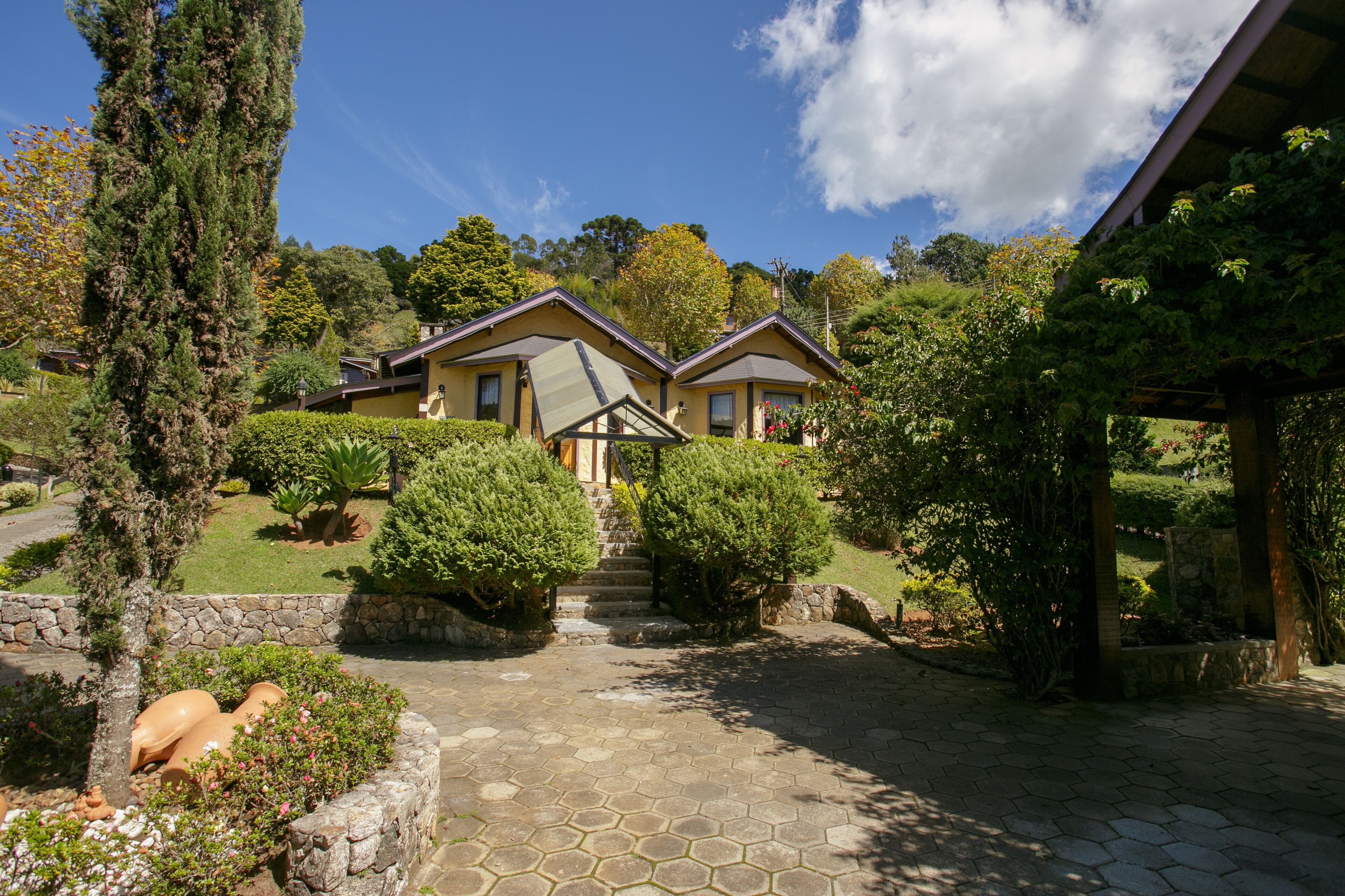 A two-story house with a stone pathway leading to the entrance, surrounded by lush greenery and a clear blue sky.