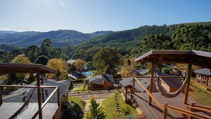 A resort with wooden deck structures, a pool, and a view of the surrounding forested hills. - Pousada Varanda das Colinas (Monte Verde)