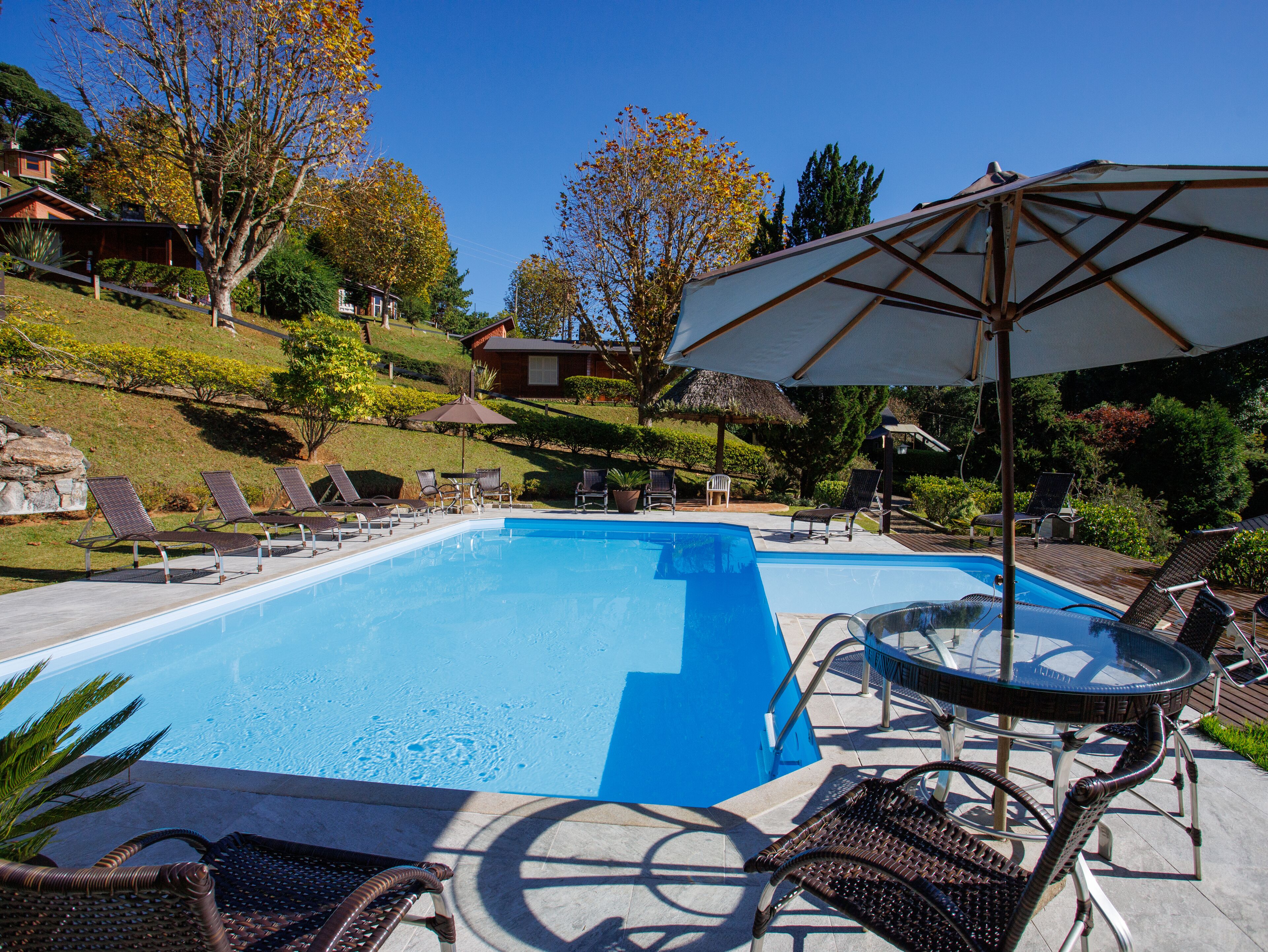 Una piscina rectangular con agua cristalina, rodeada de sillas de descanso y una mesa de vidrio.