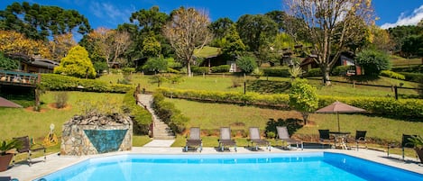 A swimming pool with lounge chairs and a stone feature, surrounded by a landscaped garden and houses in the background.