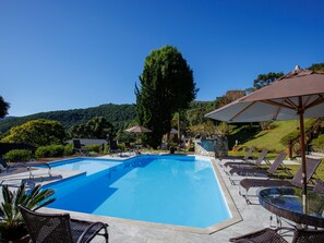 A clear blue swimming pool with lounge chairs and umbrellas, surrounded by greenery and hills. - Pousada Varanda das Colinas (Monte Verde)
