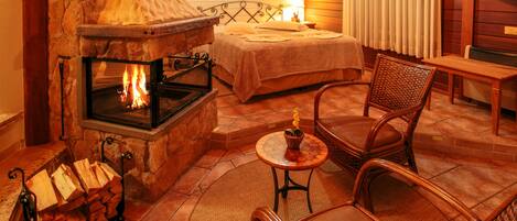 Una habitación acogedora con chimenea de piedra, una cama, una silla de mimbre y una pequeña mesa con una vela.