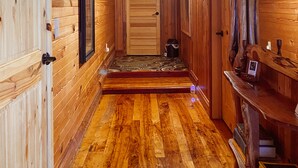 A wooden hallway with a door at the end, a small rug, and a shelf with books. - Inn at the Art Center (San Angelo)