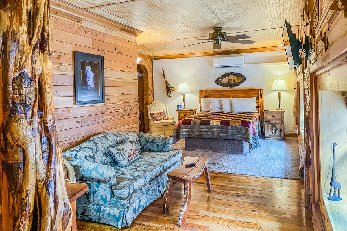 Une chambre à coucher de style chalet, avec un plafond en bois, un lit recouvert d’une courtepointe, un canapé et une petite table.