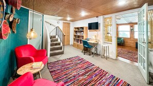 A cozy living room with a staircase, red chairs, a bookshelf, and a TV. - Inn at the Art Center (San Angelo)