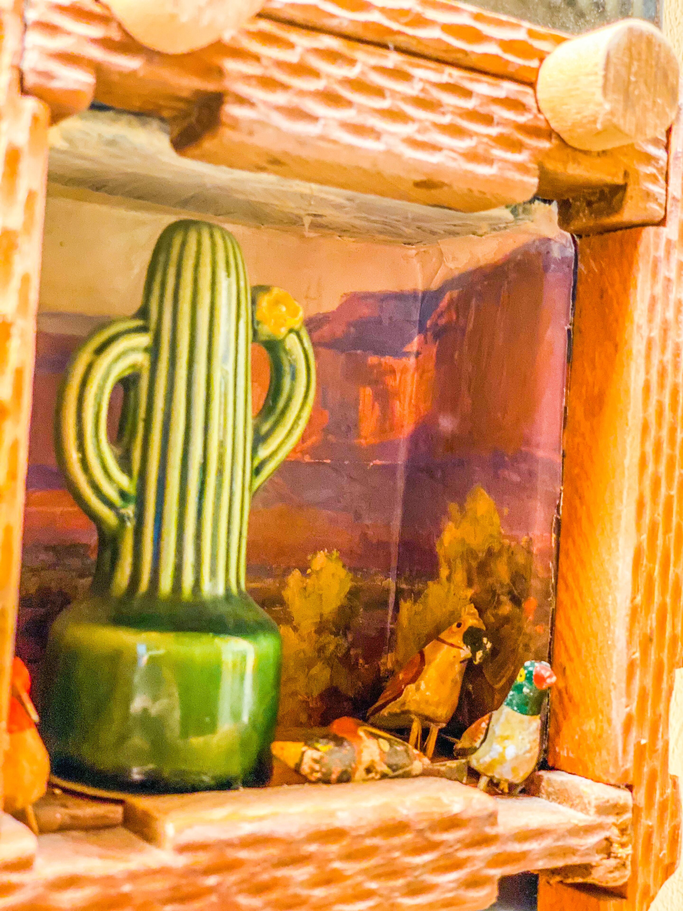 A cactus-shaped vase in a rustic wooden frame with a desert landscape painting in the background.