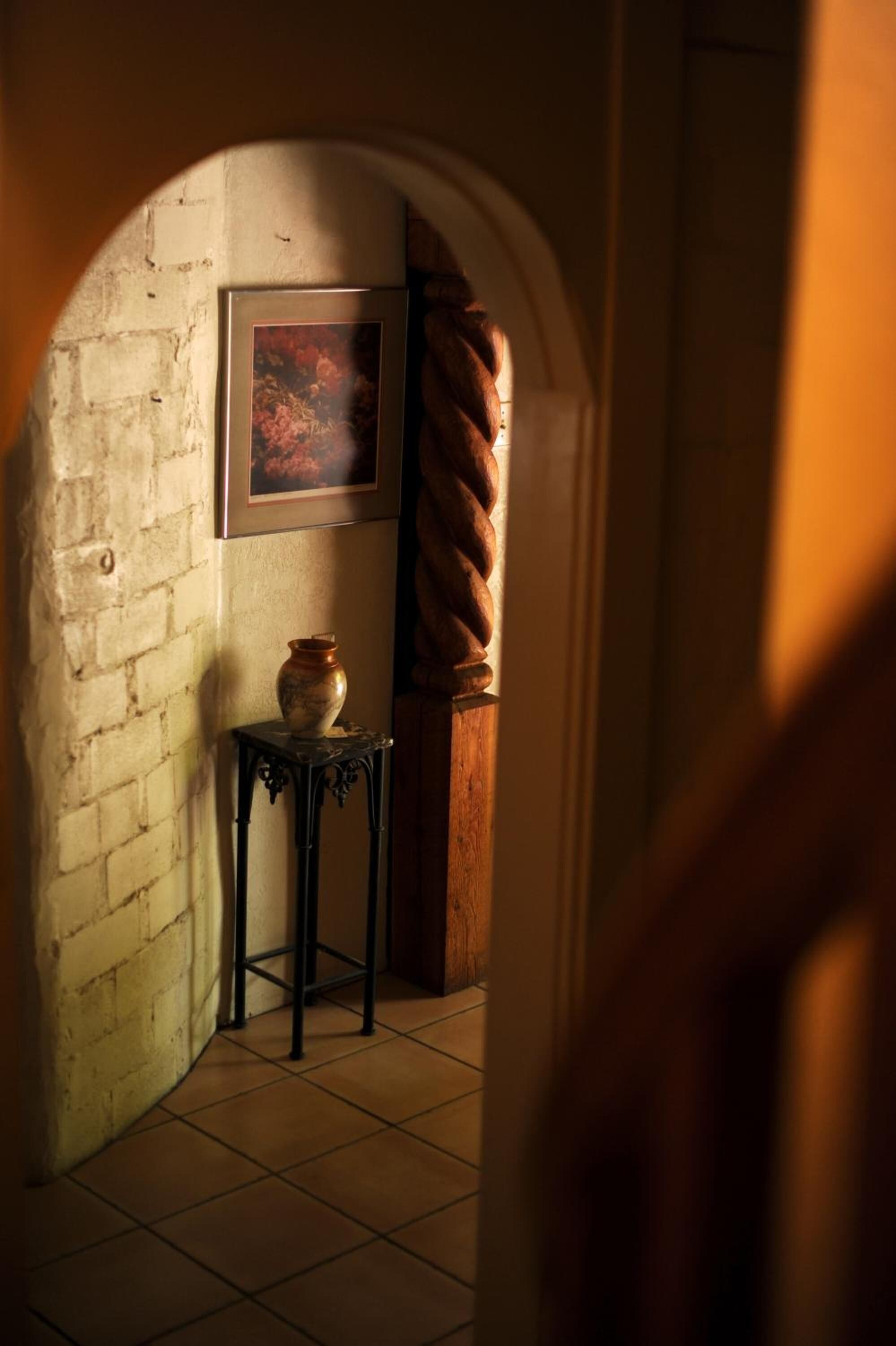 A narrow hallway with a tiled floor, a brick wall, a small table with a vase, and a framed picture on the wall.