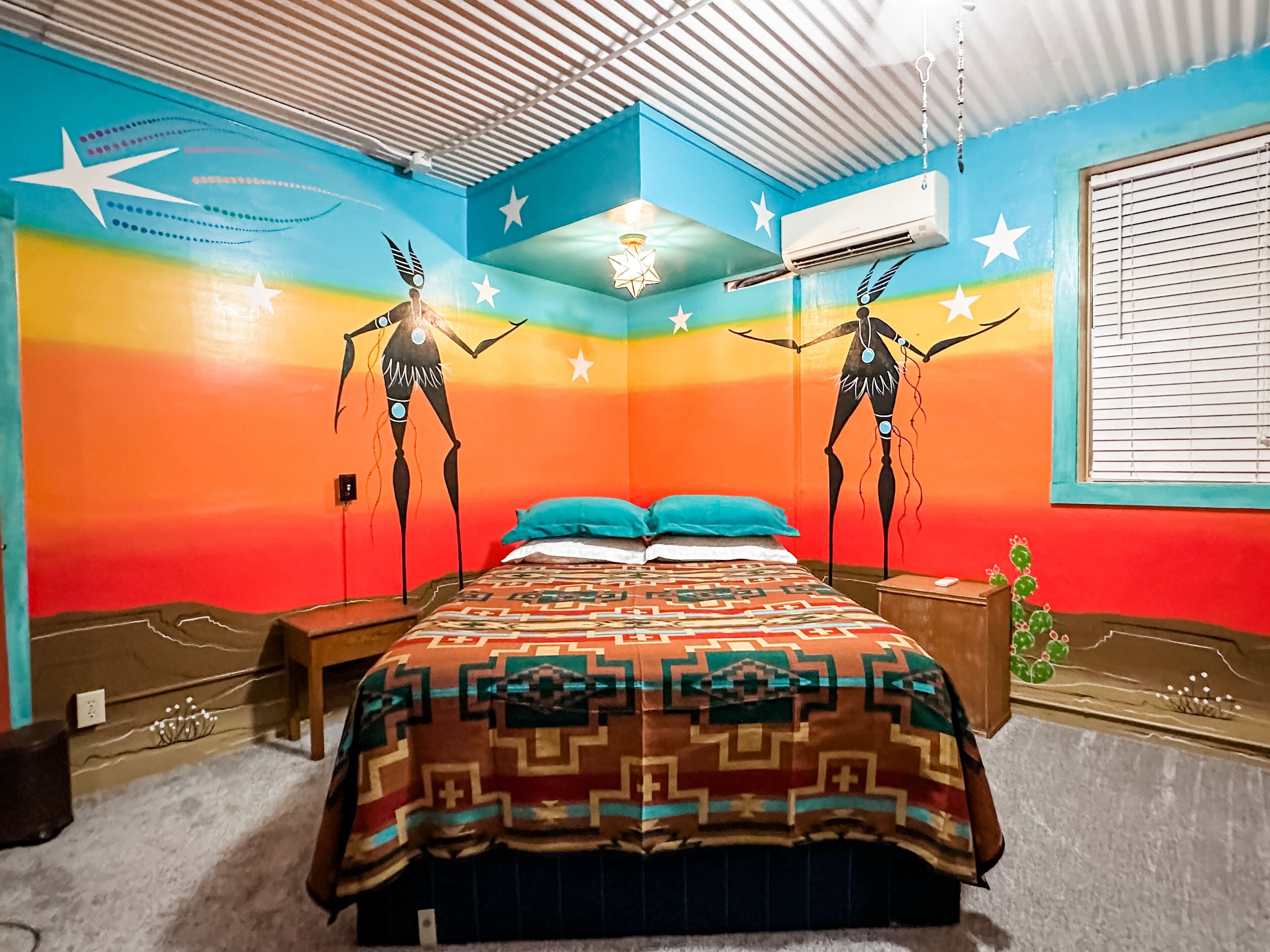 A room with a bed, a nightstand, a wall with a mural, and an air conditioning unit.
