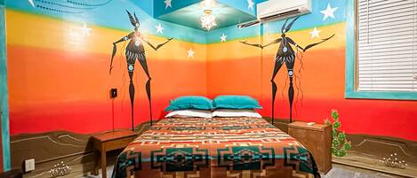 A room with a bed, a nightstand, a wall with a mural, and an air conditioning unit.