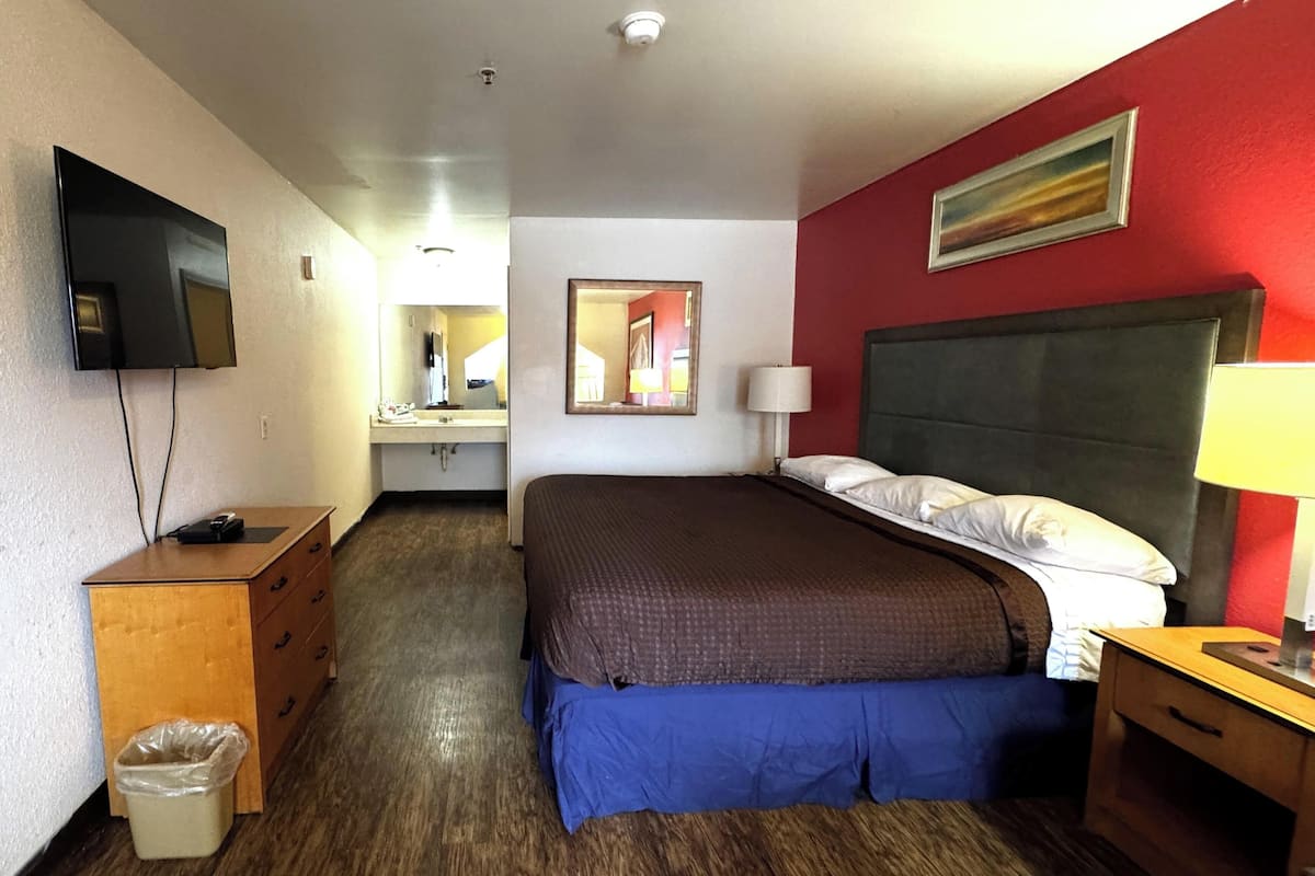 A hotel room with a bed, a desk, a TV, a mirror, and a red wall.