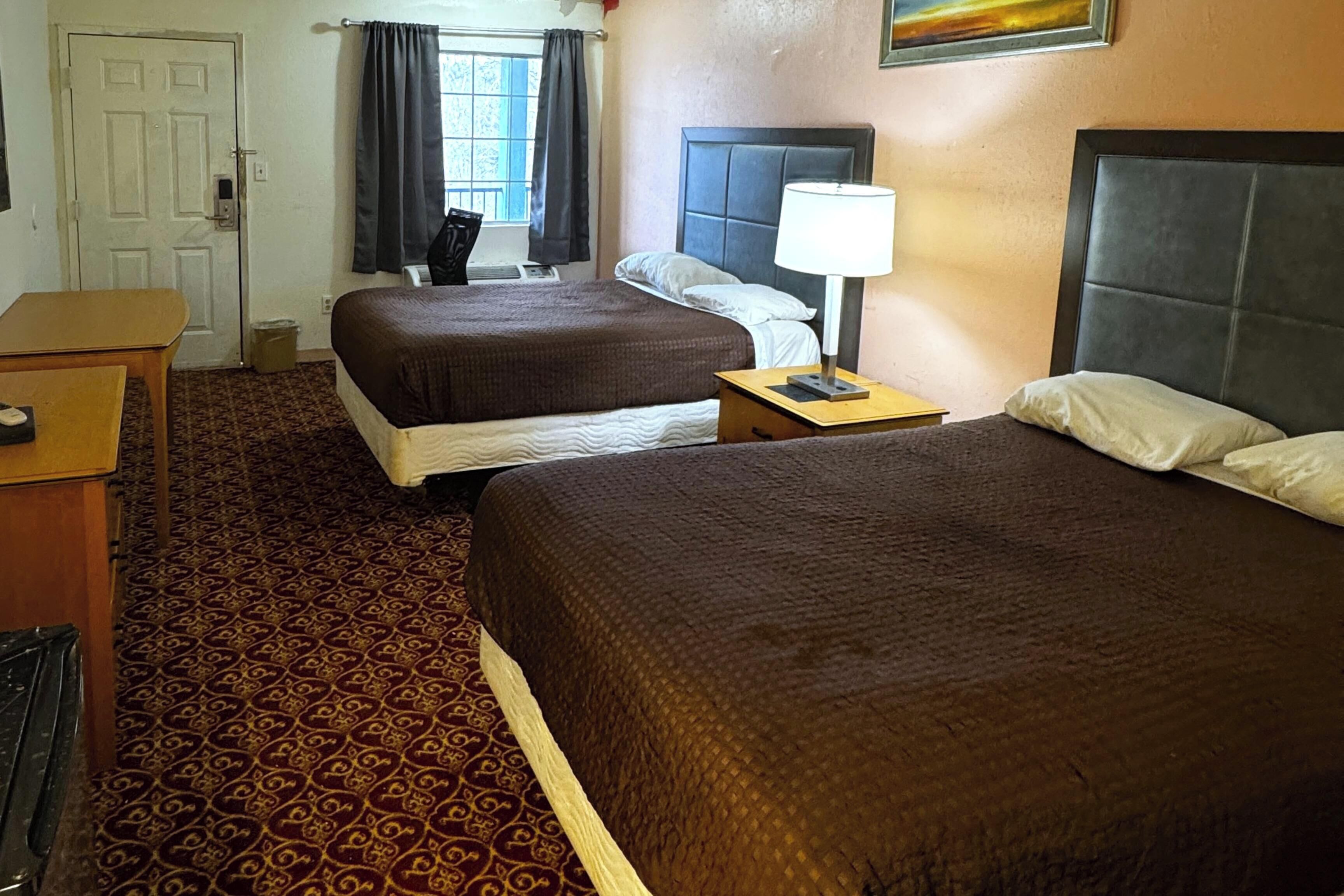Een hotelkamer met twee bedden, een bureau, een stoel, een lamp en een raam met gordijnen.