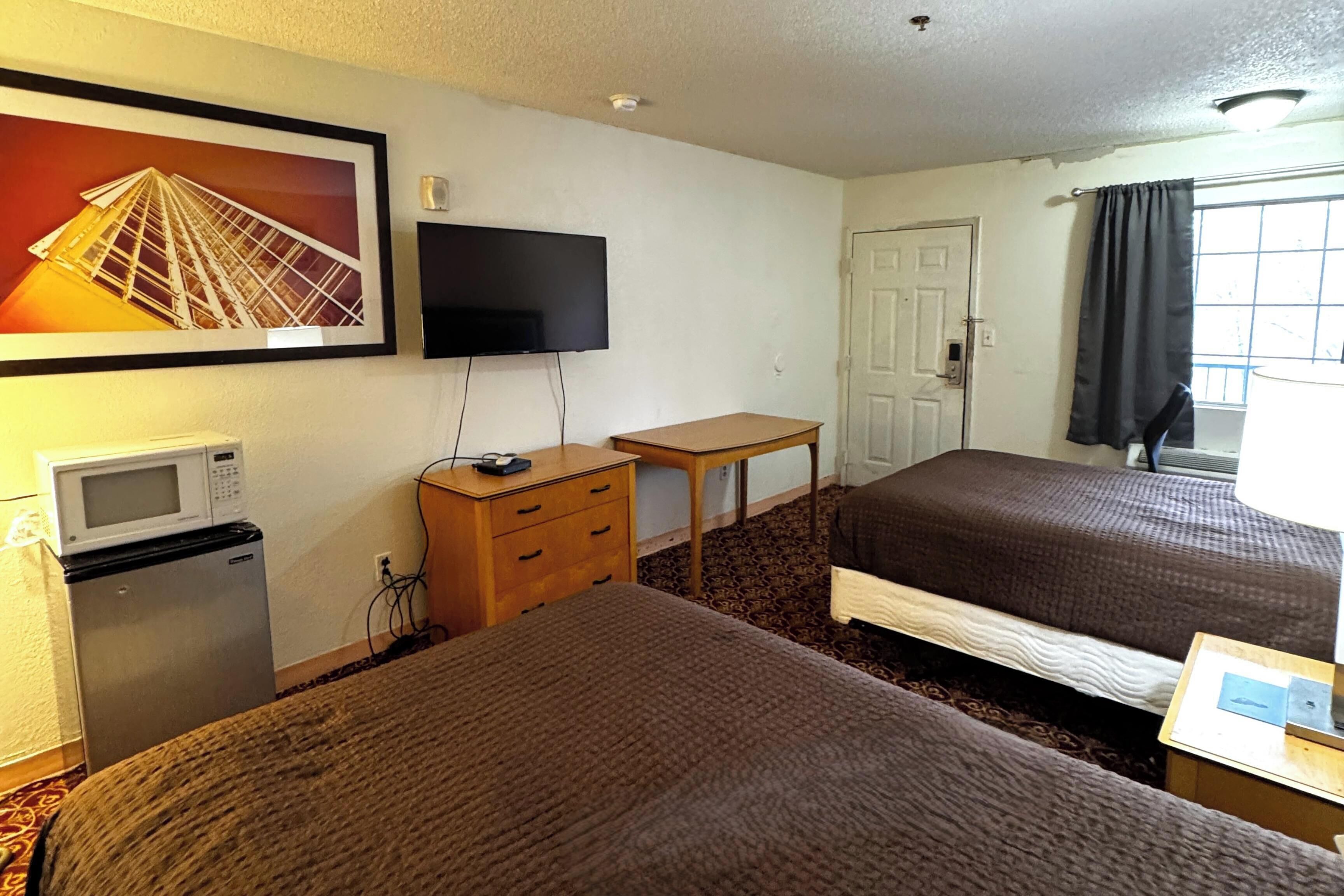 A hotel room with two beds, a television, a small desk, a microwave, and a refrigerator.