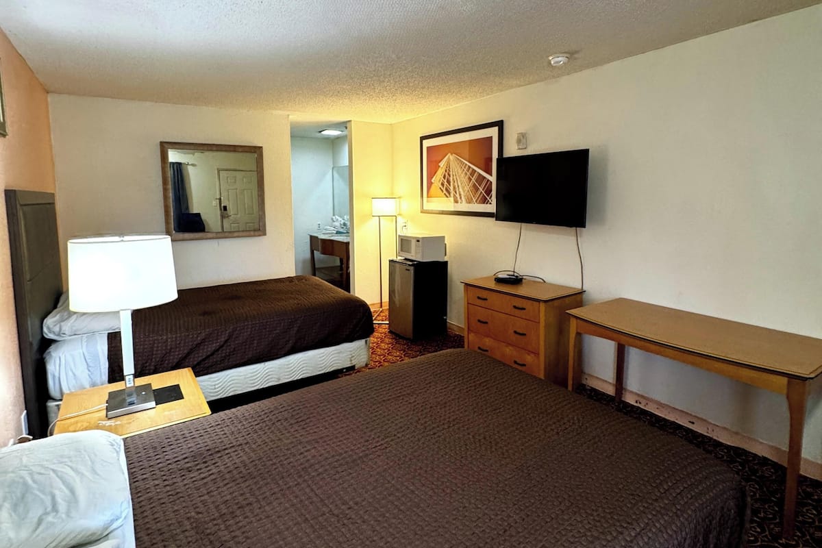 A hotel room with two beds, a desk, a television, a lamp, and a mirror.
