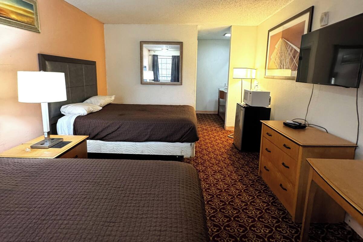 A hotel room with two beds, a desk, a dresser, a TV, and a mirror.