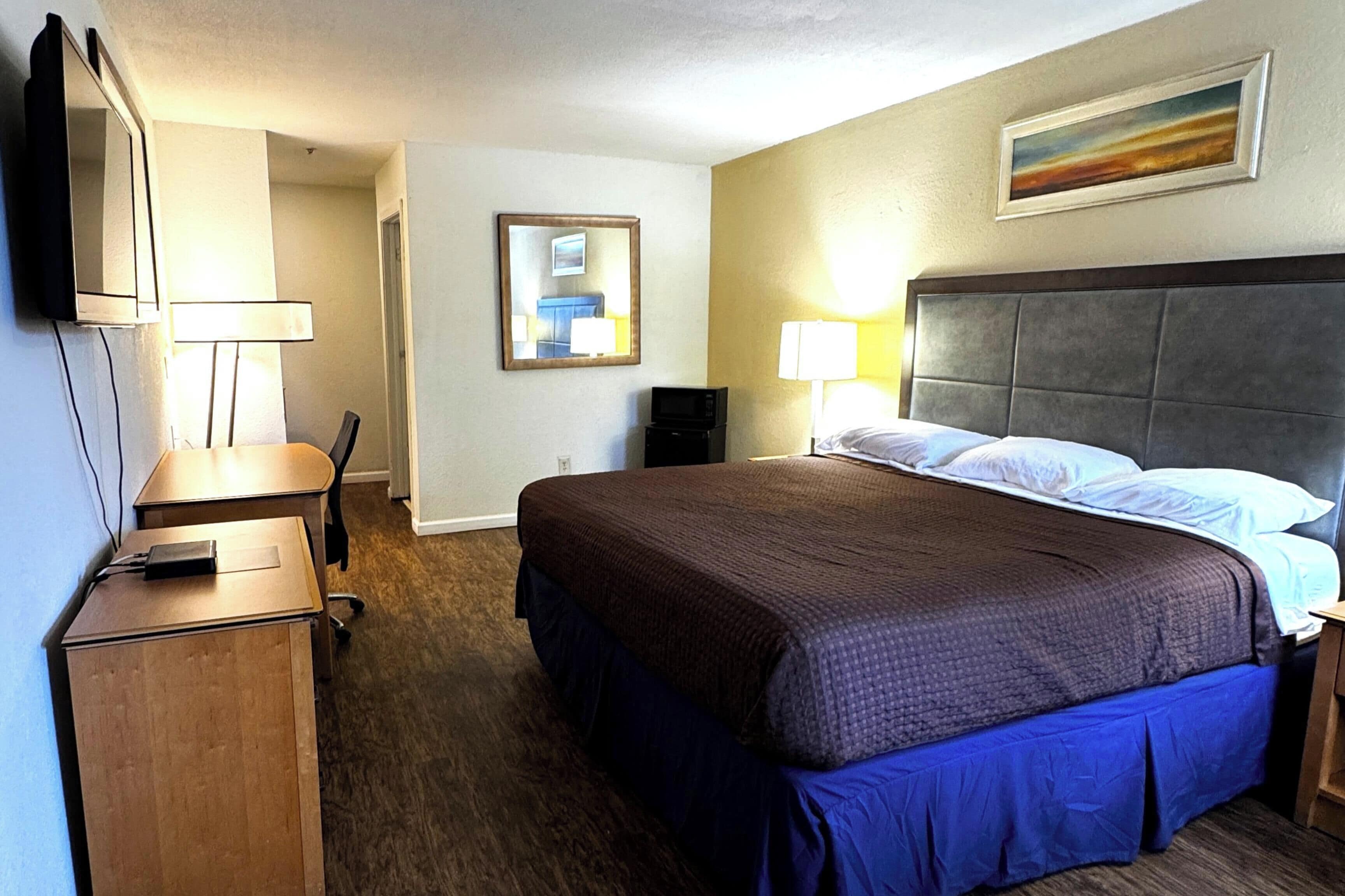 A hotel room with a large bed, bedside lamps, a flat-screen TV, a desk, and a chair.