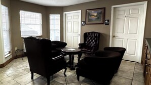 A living room with a fireplace, a black leather armchair, a round coffee table, and a view of the outside through a window.