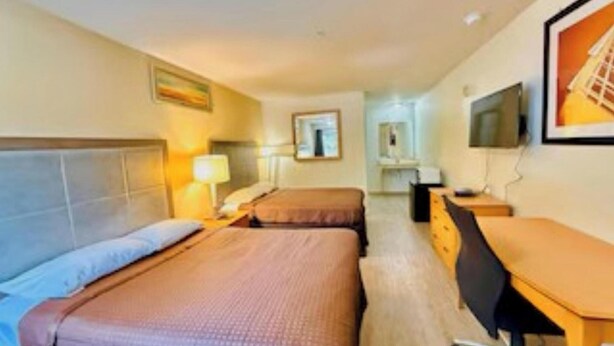 A hotel room with two beds, a desk, a chair, a TV, and a mirror.