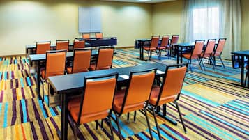 A conference room with multiple tables and chairs, carpeted floor, and a projector screen on the wall.