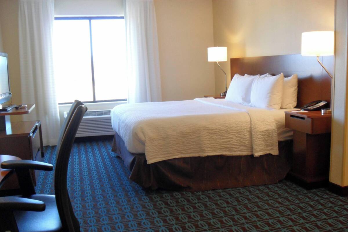 Habitación de hotel con cama, escritorio con silla, teléfono y ventana con cortinas.