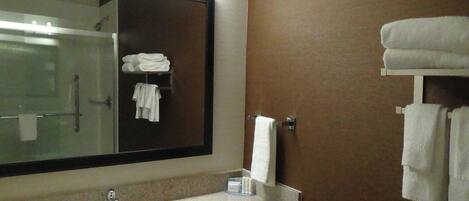 A bathroom with a large mirror, a sink, and a towel rack with folded towels.