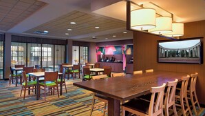 A hotel dining area with a large wooden table, multiple chairs, and a colorful carpet.