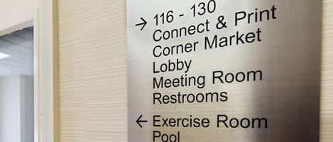 A directional sign with arrows pointing to various facilities including a Connect & Print area, Corner Market, Lobby, Meeting Room, Restrooms, Exercise Room, Pool, Ice, and another Restroom.