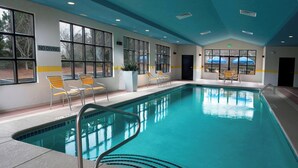 An indoor swimming pool with clear blue water, yellow and white chairs, and large windows.