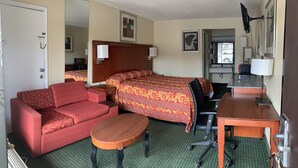 A hotel room with a bed, a red sofa, a wooden desk, a chair, a small table, and a mirror. - Night Inn (Rowland)