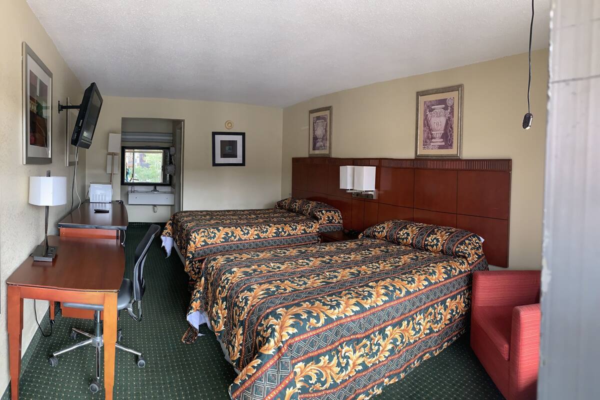 A hotel room with two beds, a desk, a chair, a TV, and a window.
