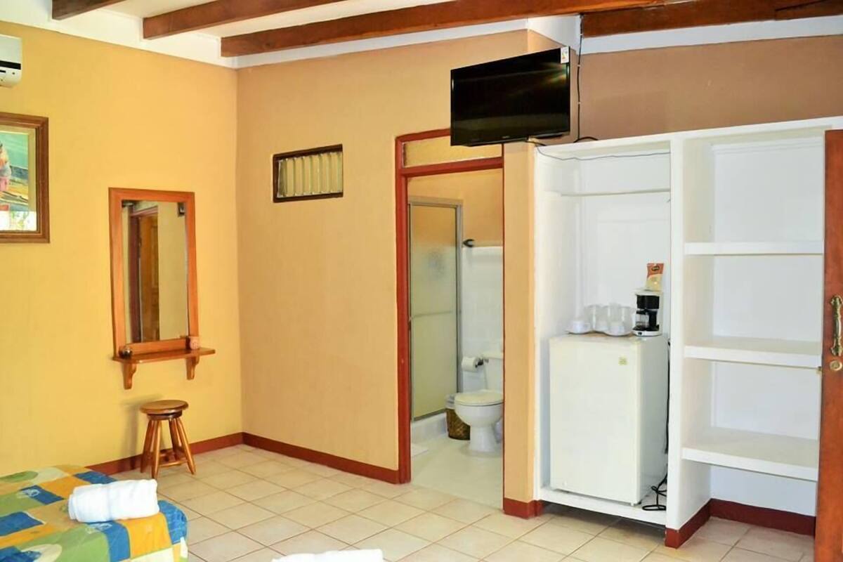 A hotel room with a bed, a television, a wardrobe, a bathroom, and a small stool.