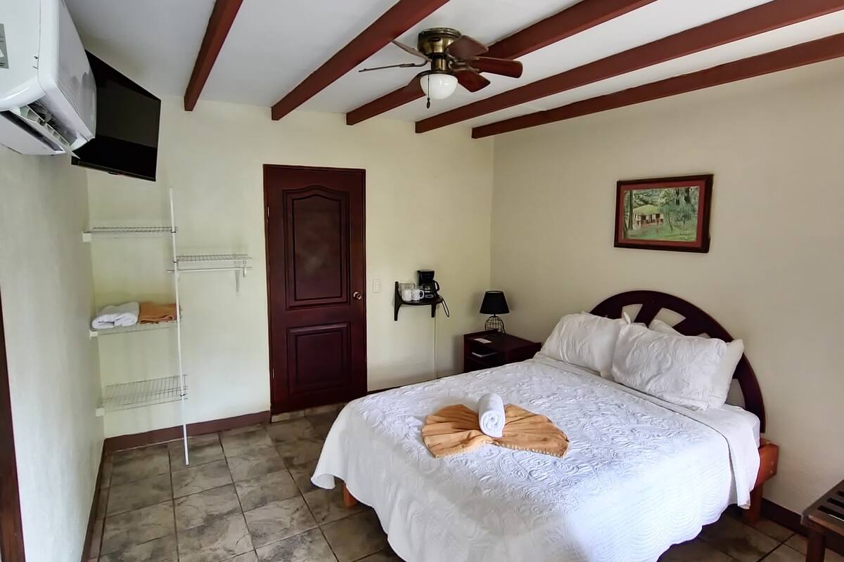 A bedroom with a bed, a ceiling fan, a door, and a wall-mounted shelf.