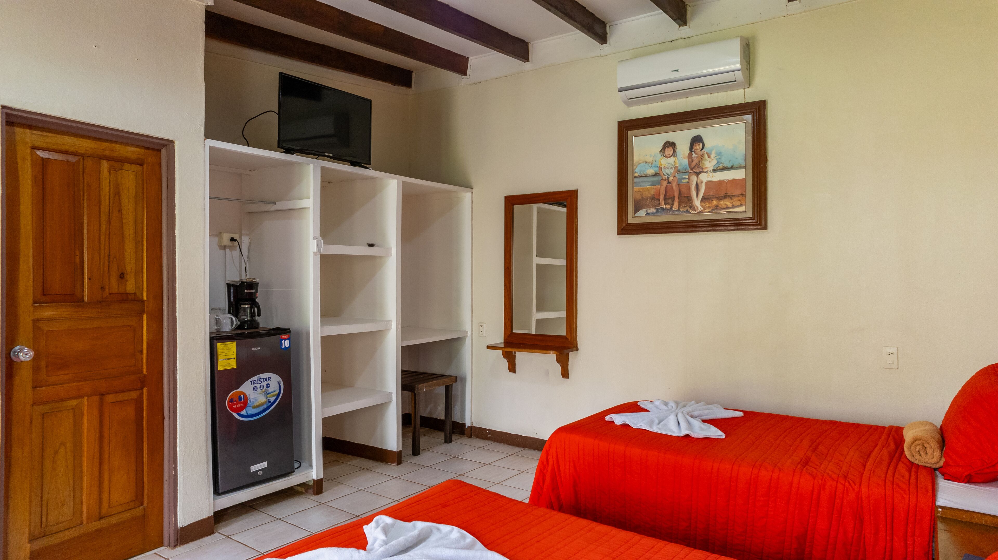 Une chambre d’hôtel avec deux lits, un minibar, une télévision, un tableau et un appareil de climatisation.