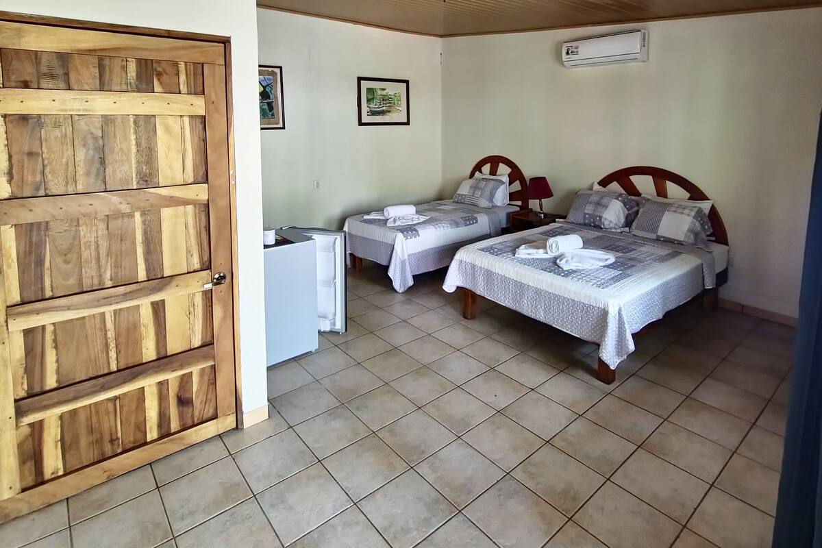 A room with two beds, a wooden ceiling, a tiled floor, and a door.